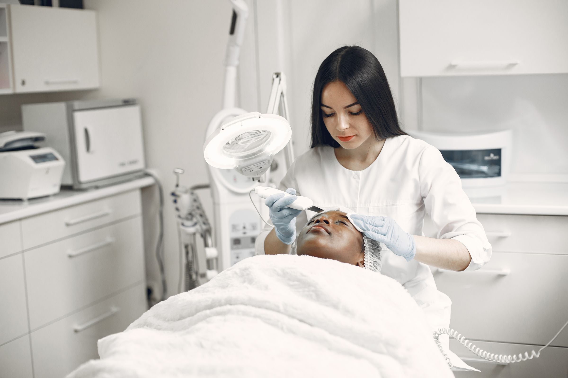 Profissional de estética realizando um procedimento facial em uma paciente na maca