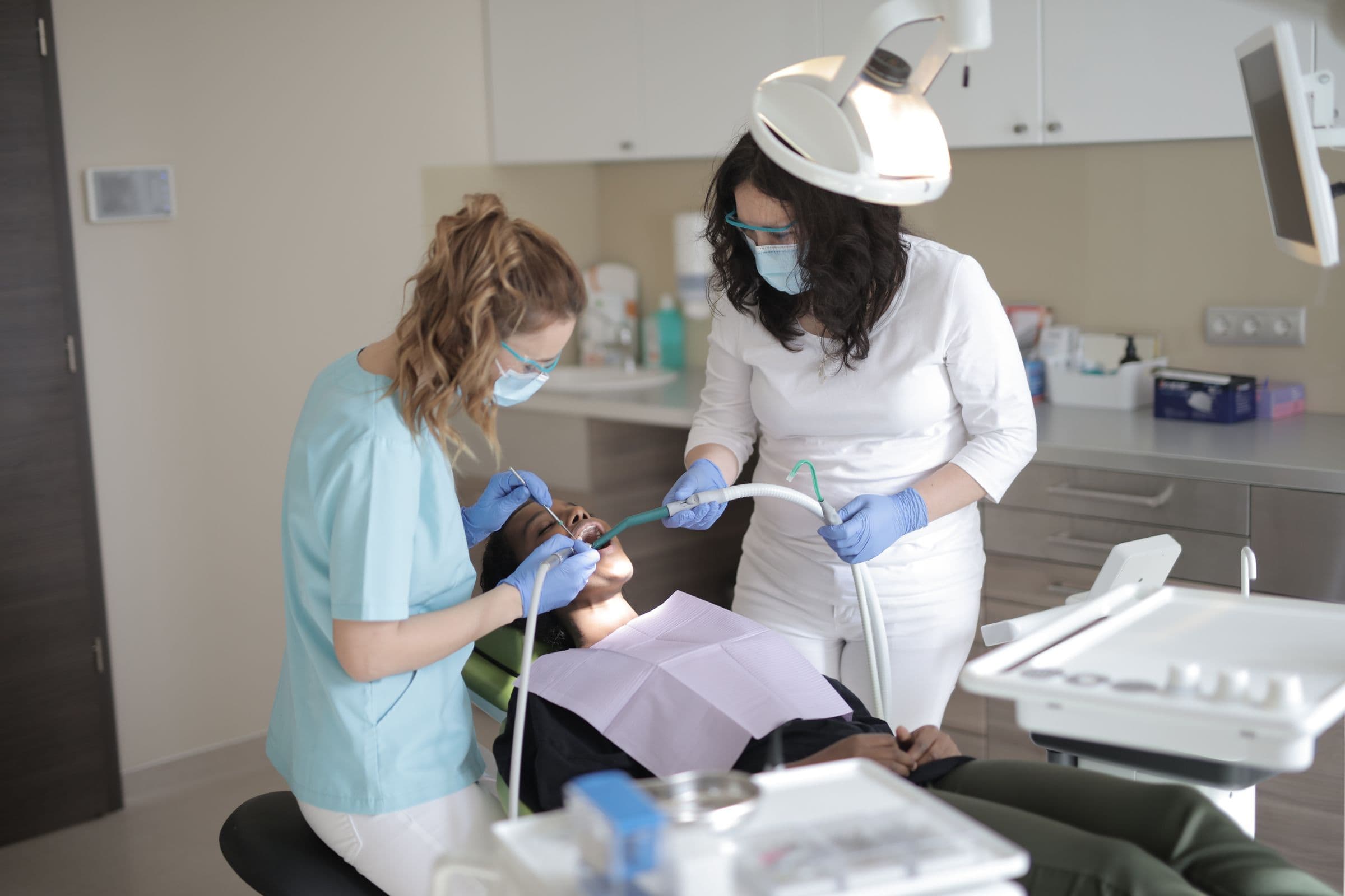 Dentista e auxiliar atendendo uma paciente na cadeira do consultório odontológico